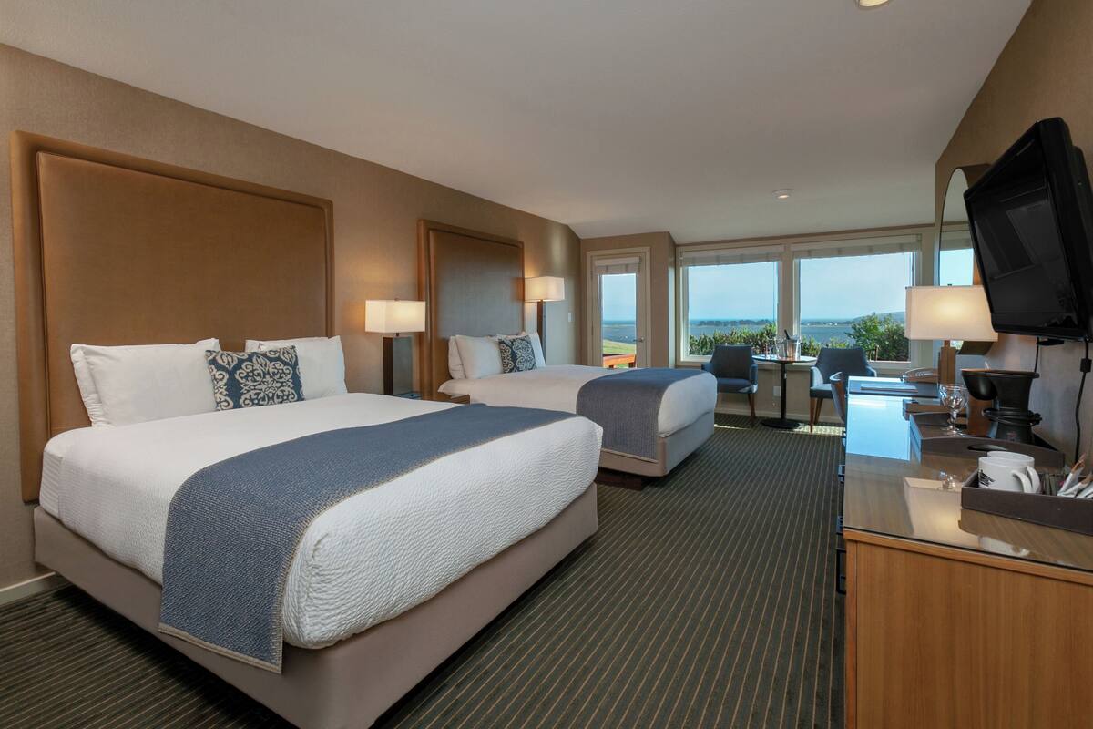 A hotel room with two beds, a desk with a television, and a view of the outdoors.