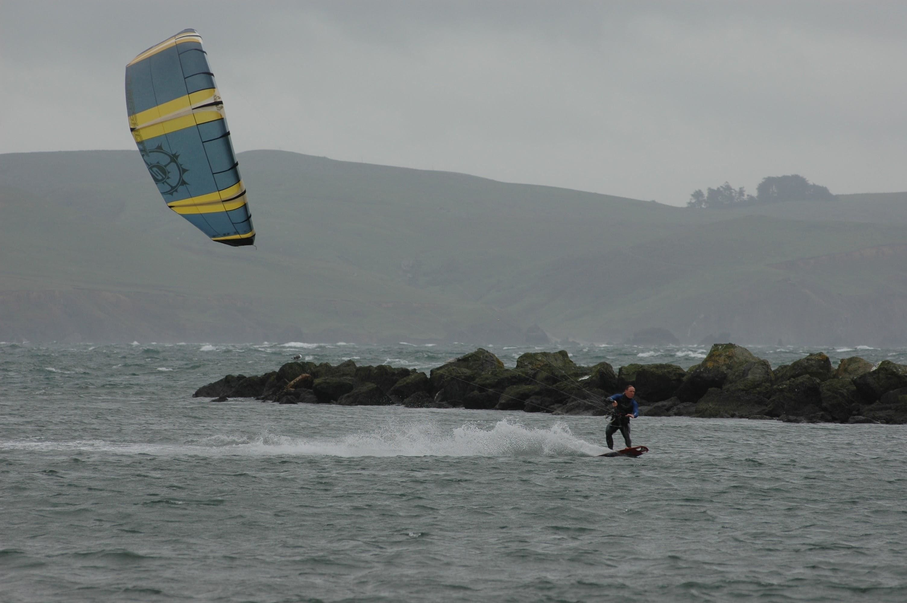 Una persona practicando windsurf en un cuerpo de agua, con una cometa grande.