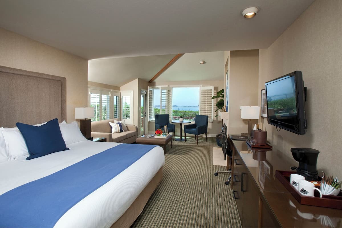 A hotel room with a large bed, a TV, a desk with a computer, and a view of the sea.