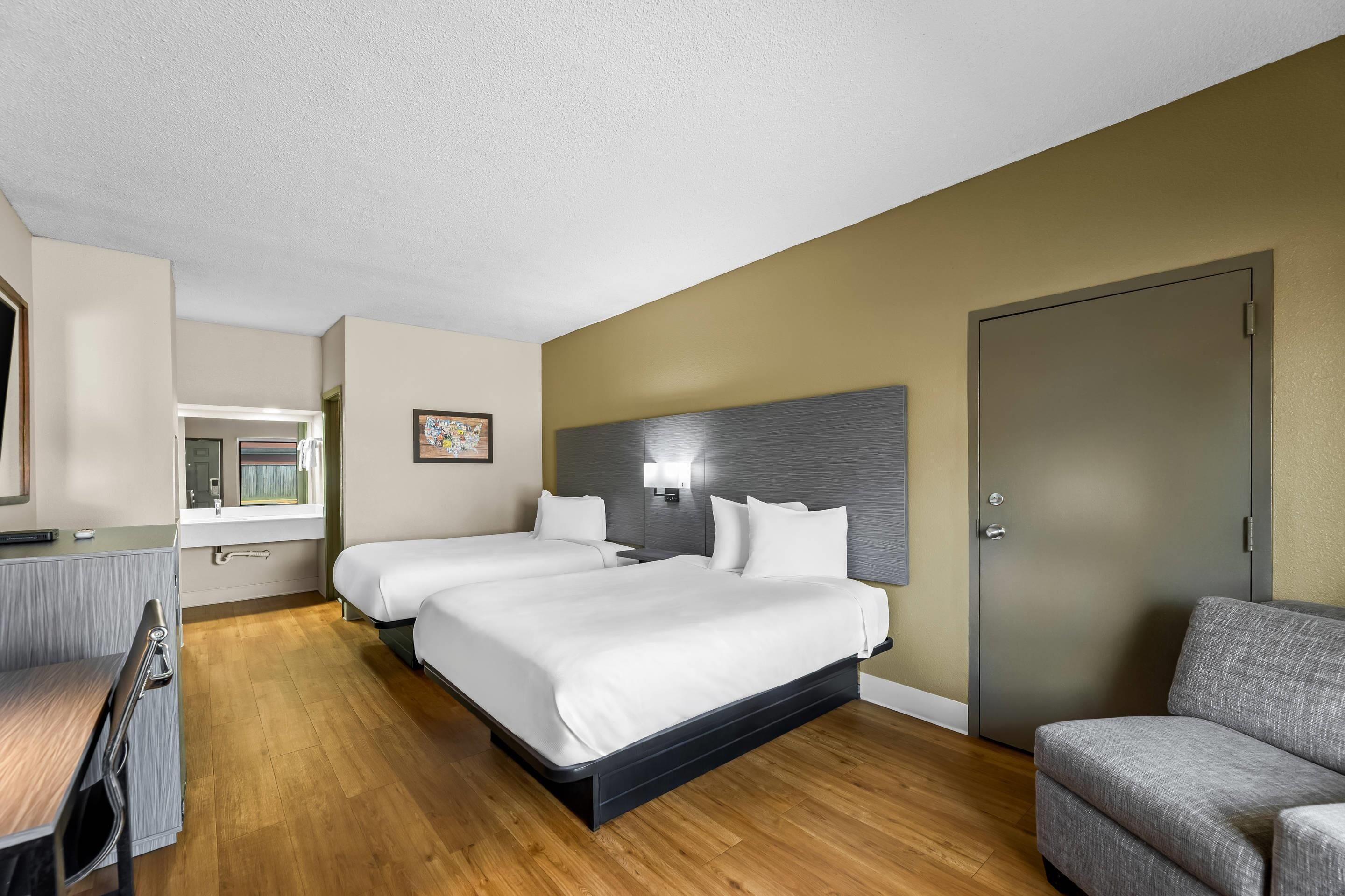 Habitación de hotel con dos camas, un escritorio, una silla, un sofá y una puerta.