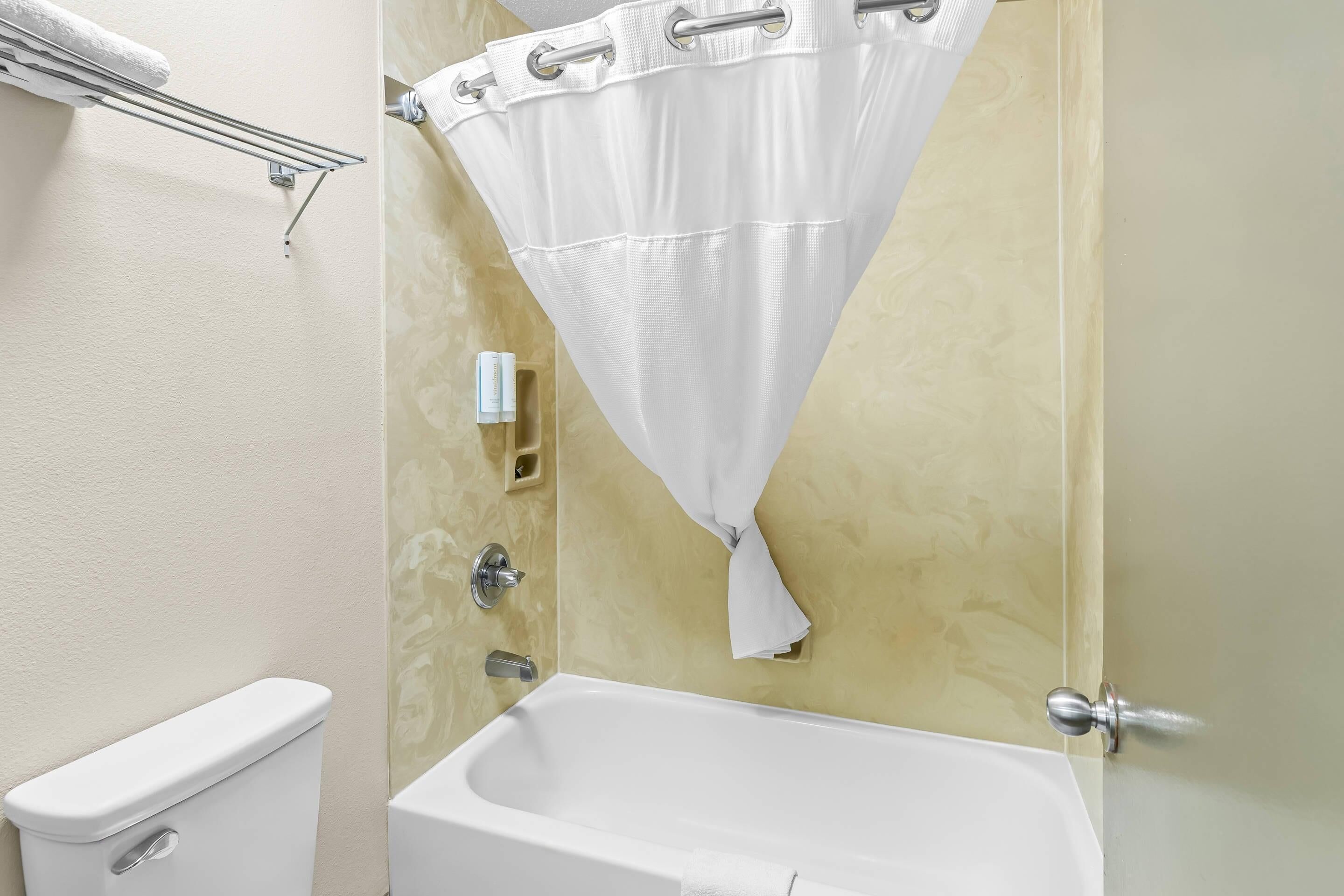 Une salle de bain équipée de toilettes, d’une baignoire, d’un rideau de douche et d’un porte-serviettes.
