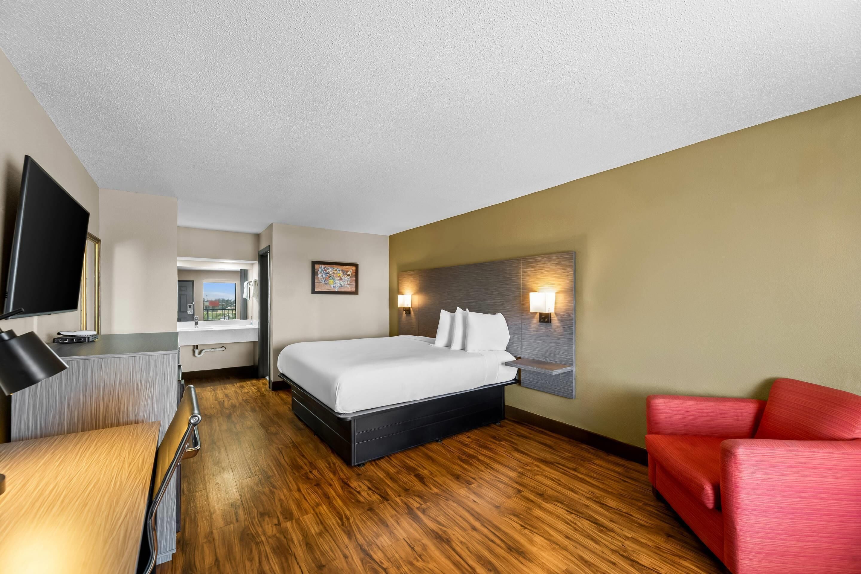 A hotel room with a bed, a desk, a chair, a TV, and a red sofa.