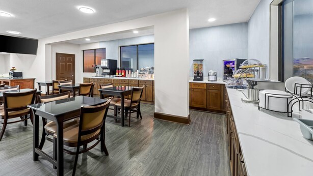 Un espace repas moderne dans un hôtel, avec une grande table et des chaises, un coin cuisine équipé d’appareils électroménagers et une grande fenêtre offrant une vue panoramique.