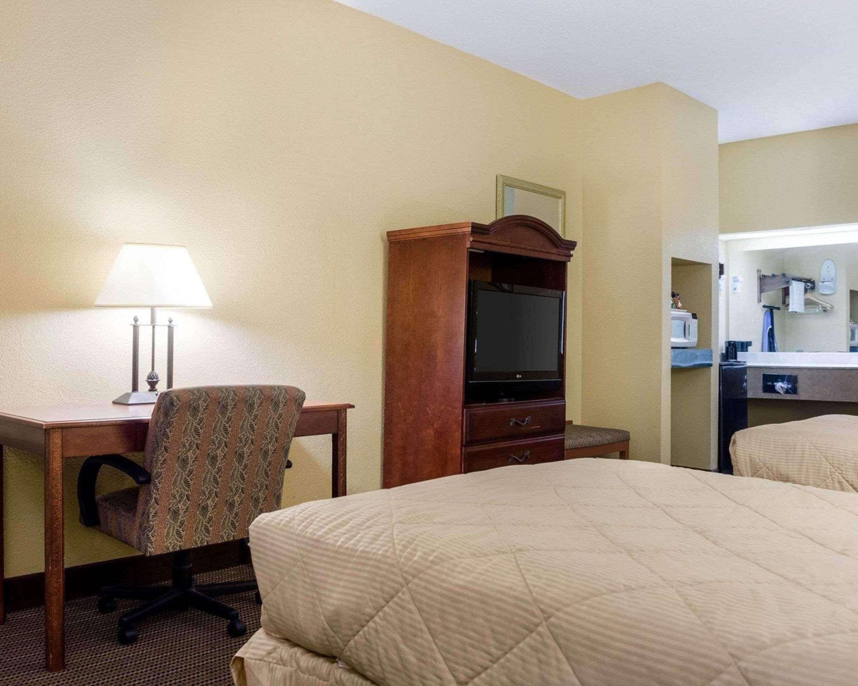 A hotel room with a bed, a desk with a lamp, a television, and a dresser.