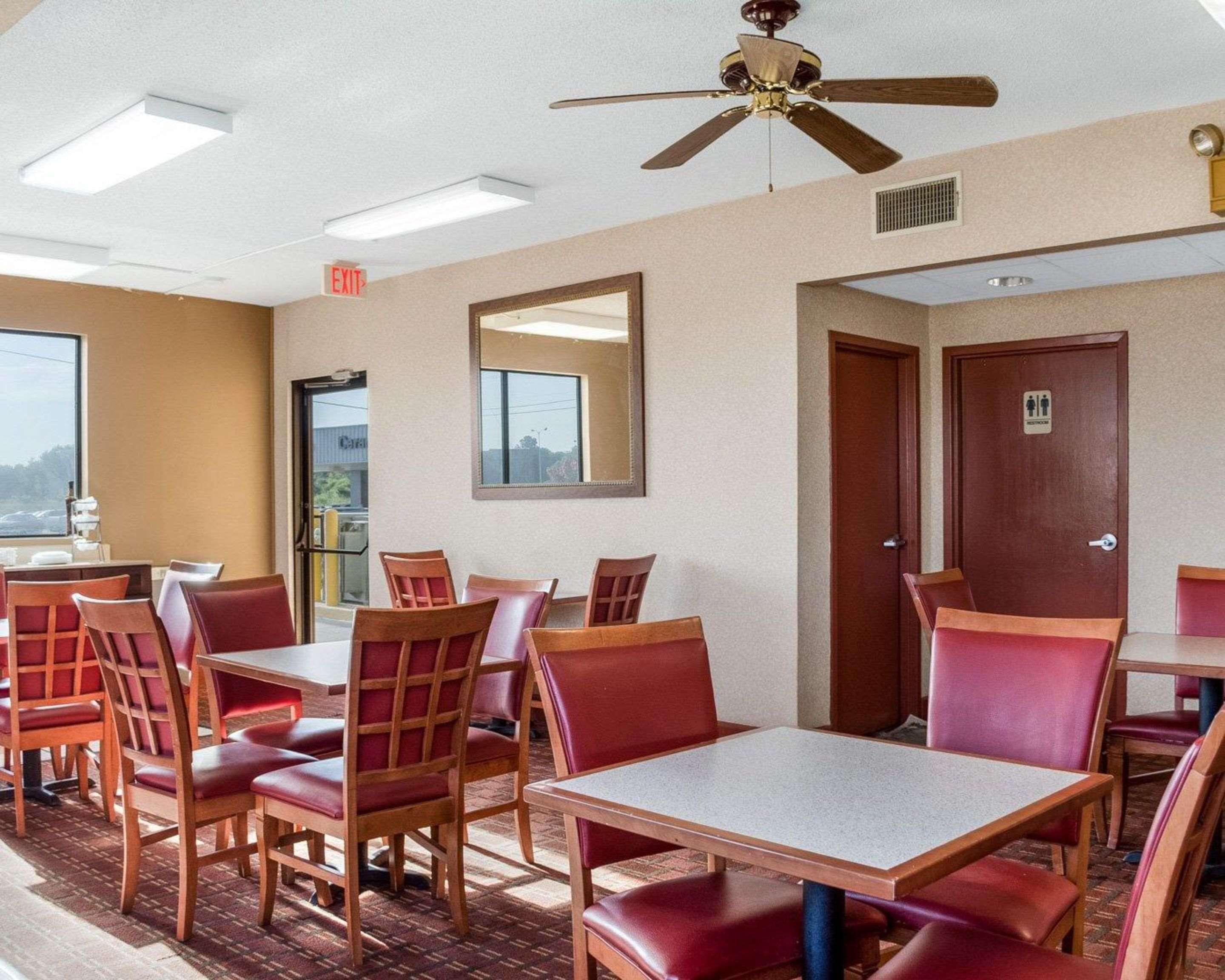 A hotel dining area with tables and chairs, a ceiling fan, and an exit sign.