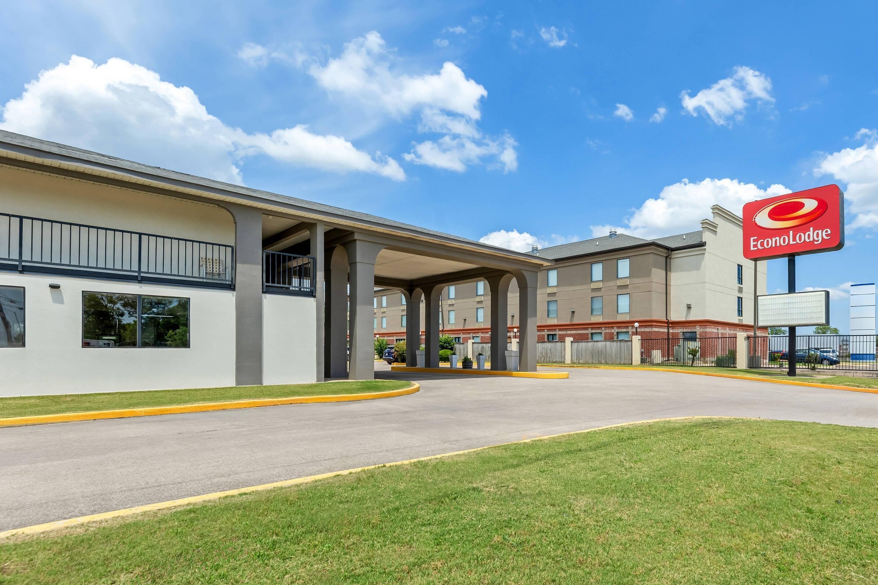 Un hotel con un área exterior techada, aparcamiento y cielo despejado.