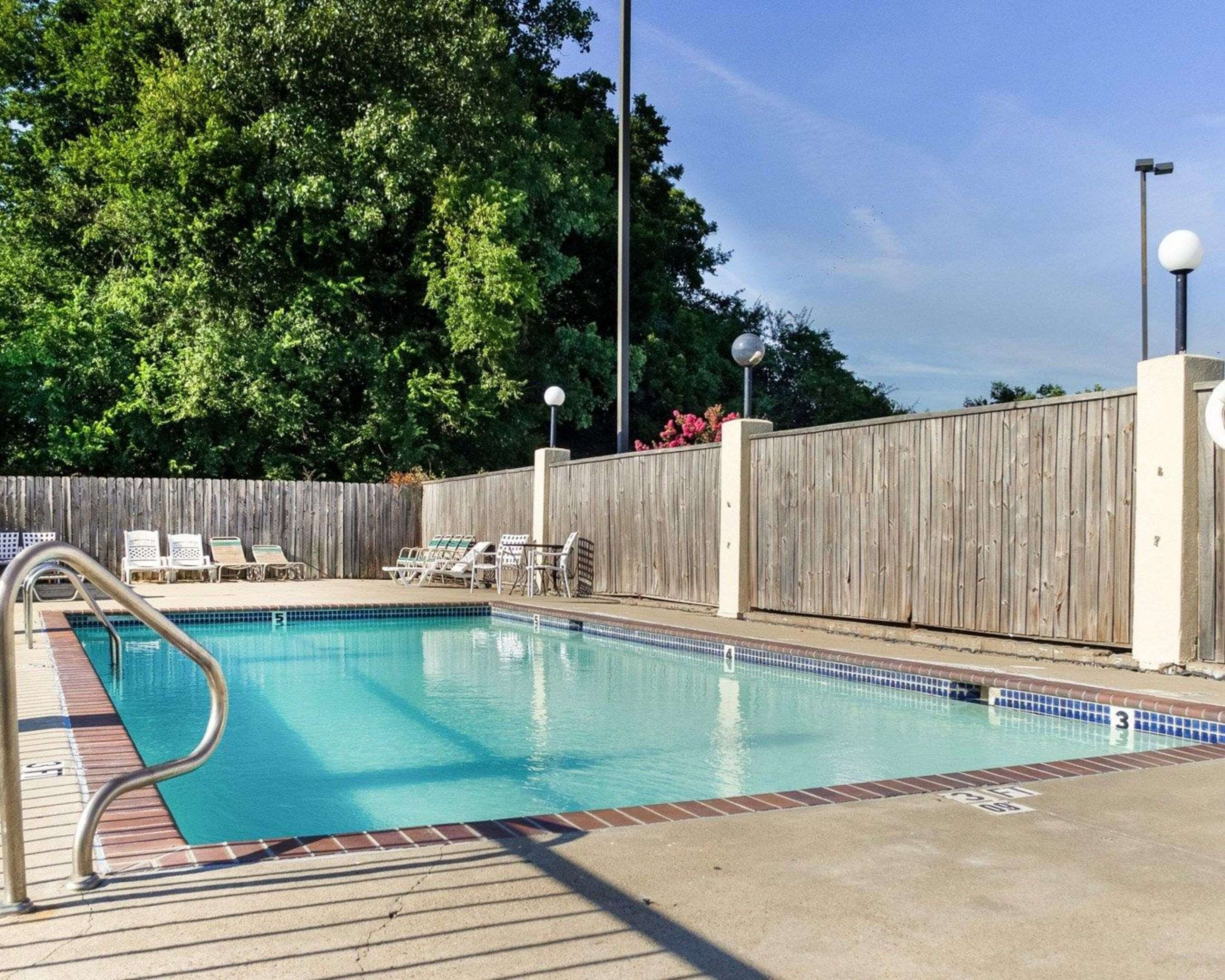 A swimming pool with a wooden fence, lounge chairs, and a metal ladder.