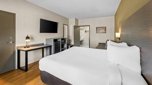 Une chambre d’hôtel avec un lit, un bureau, une télévision, un miroir et une porte.