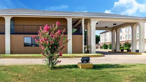 Un hôtel doté d’une entrée couverte, d’un petit jardin agrémenté de fleurs roses et d’un porte-bagages.