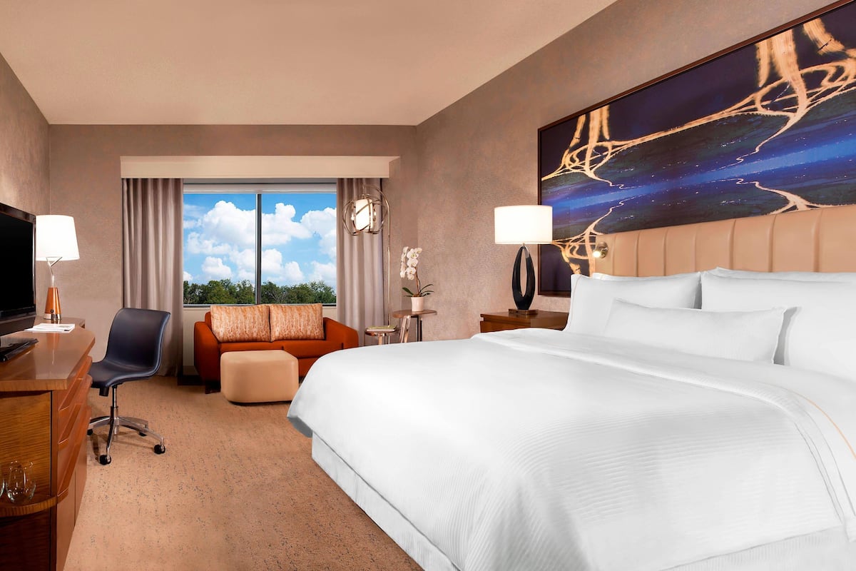 Habitación de hotel con una cama grande, un escritorio con silla, un sofá, un televisor y una ventana con vistas al cielo.