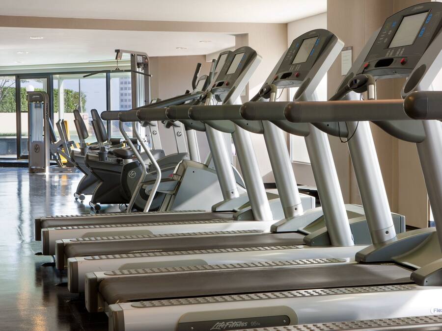 Varias cintas de correr en un gimnasio, con un muro de cristal al fondo.