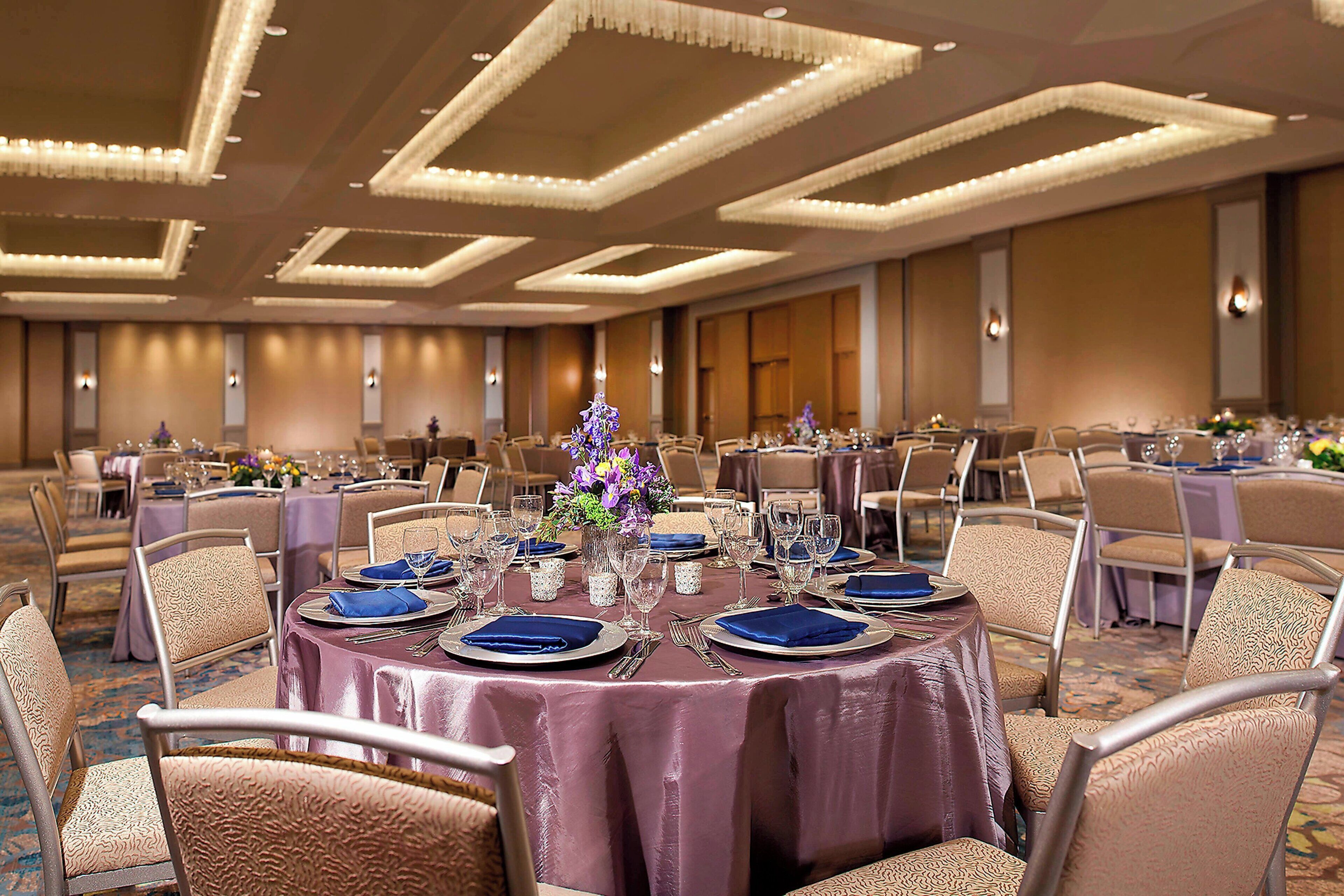 A banquet hall with round tables set for dining, featuring a central floral arrangement.