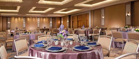 A banquet hall with round tables set for dining, featuring a central floral arrangement.
