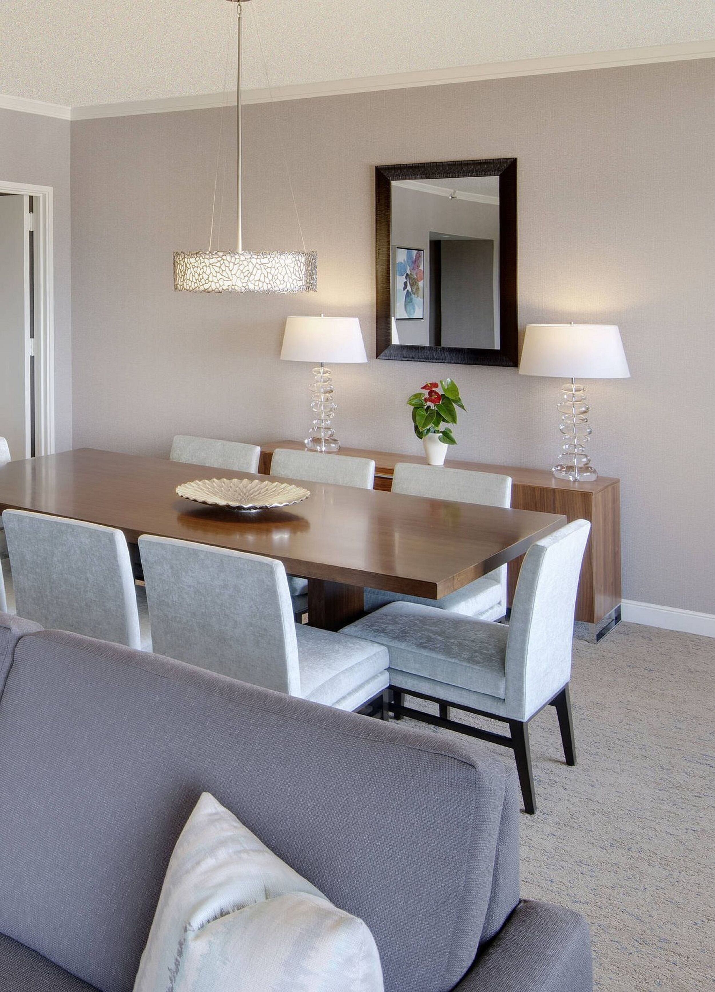 A dining area with a wooden table, grey upholstered chairs, and two floor lamps.