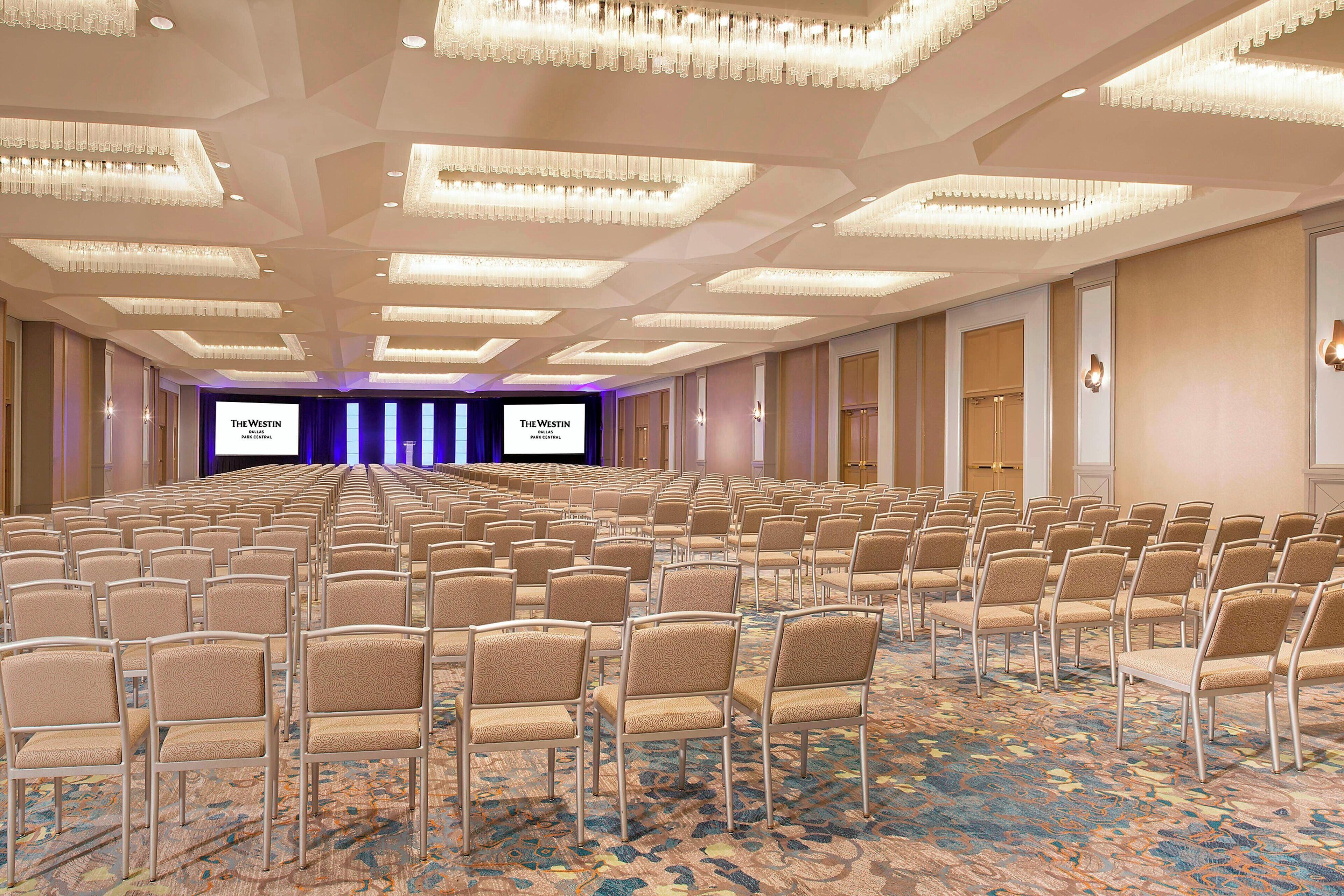 A large conference room with rows of chairs and a stage with a screen.
