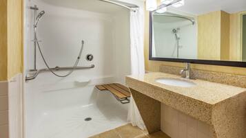 A modern bathroom with a walk-in shower, grab bars, a sink with a granite countertop, and a large mirror.