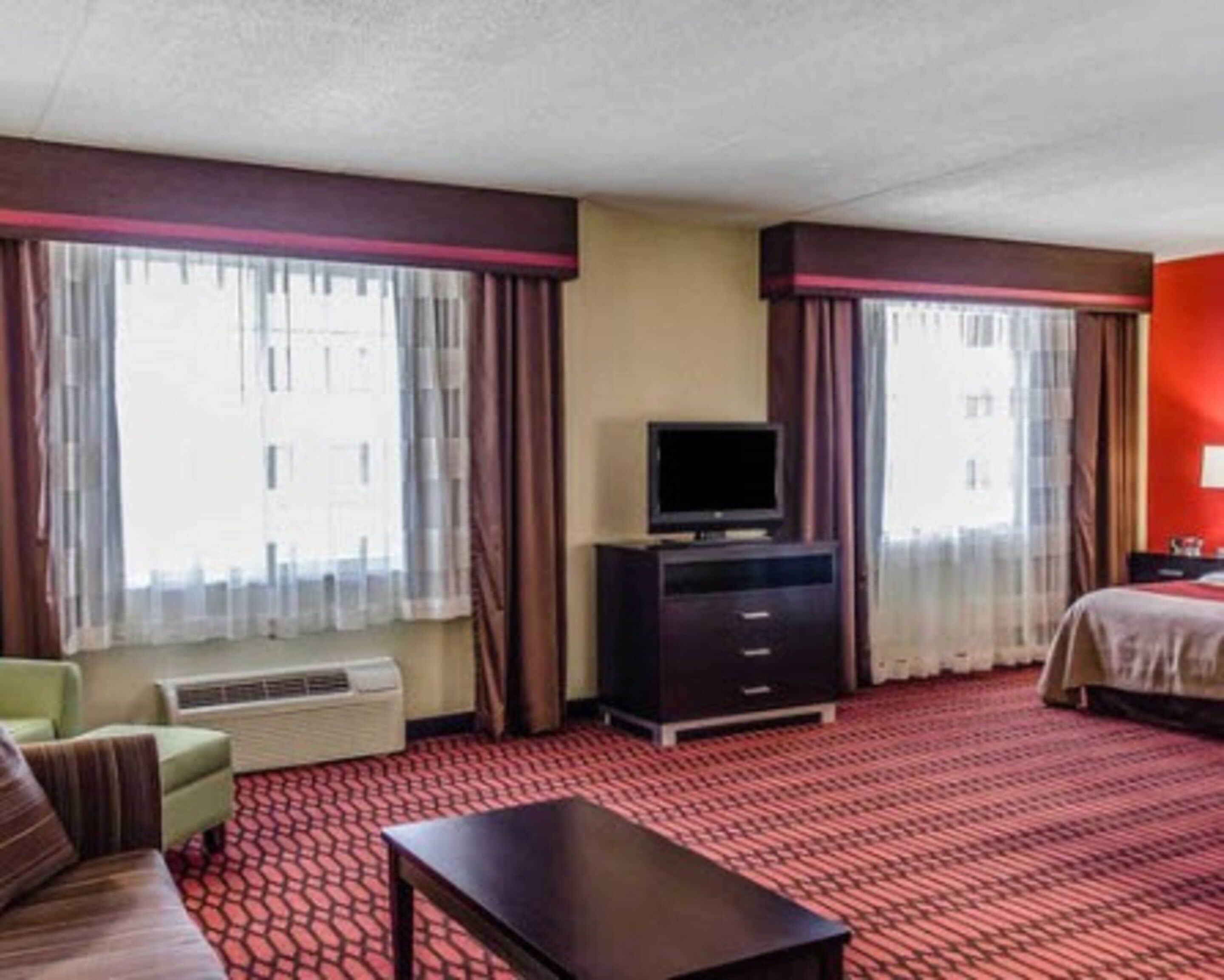 A hotel room with a bed, a television on a stand, a sofa, and a carpeted floor.