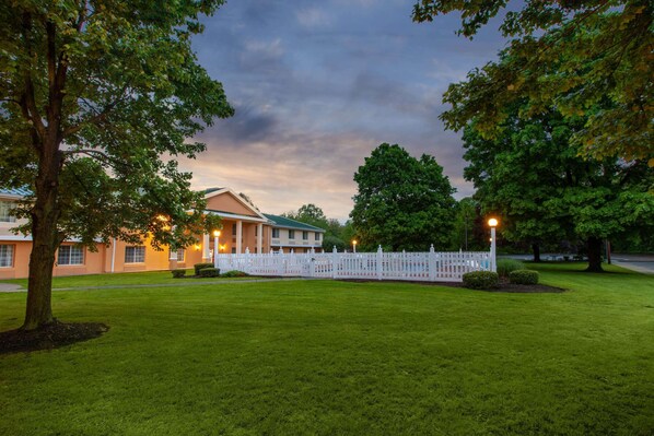 A building with a white fence, green lawn, and trees. - Baymont by Wyndham Harrisburg (Harrisburg)