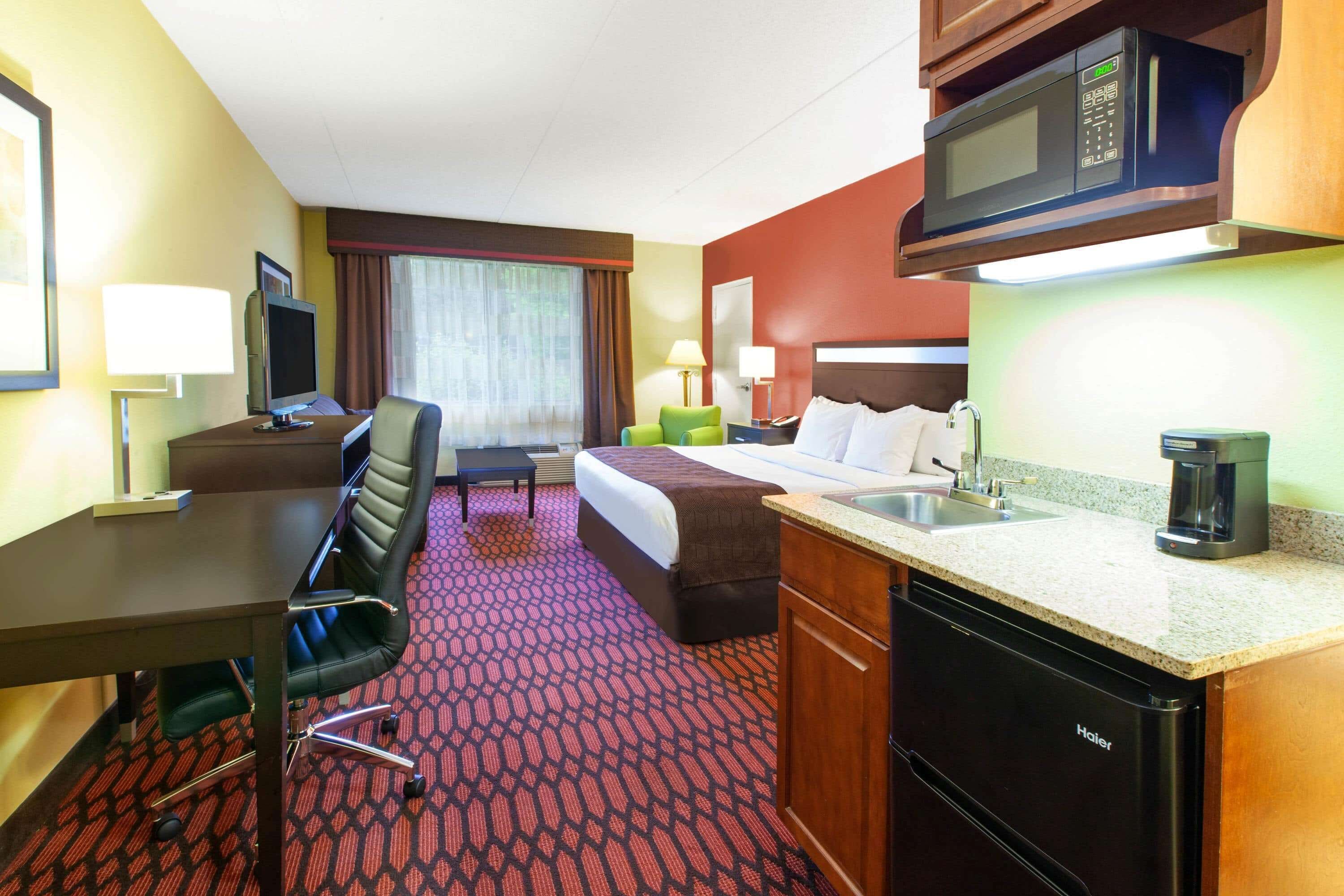 Una habitación de hotel con cama, escritorio, silla, kitchenette y televisor.