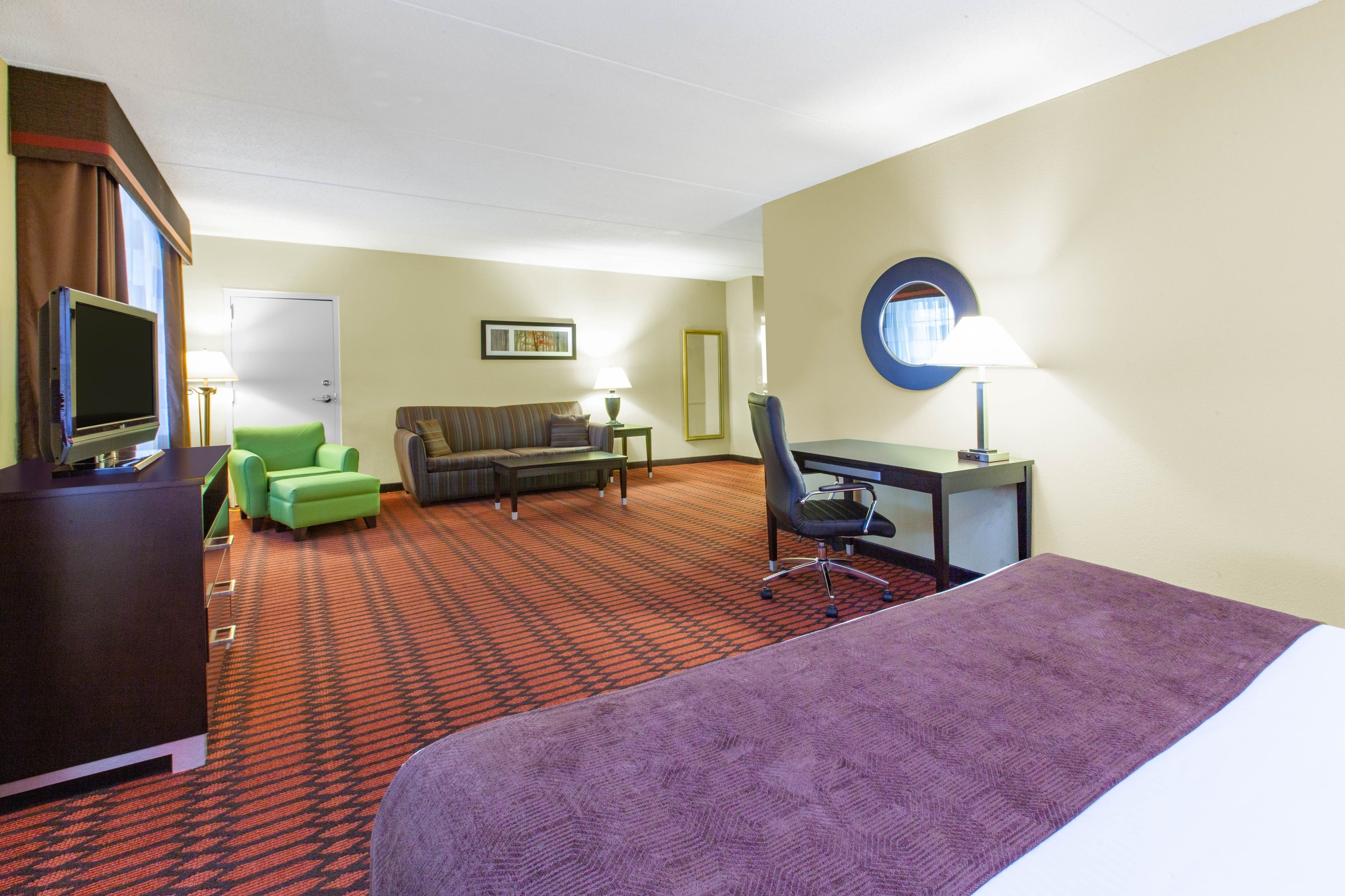 Une chambre d’hôtel comprenant un lit, un bureau, une chaise, un canapé, un téléviseur et un sol recouvert de moquette.