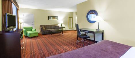 Quarto de hotel com cama, escrivaninha, cadeira, sofá, televisão e piso coberto por carpete.