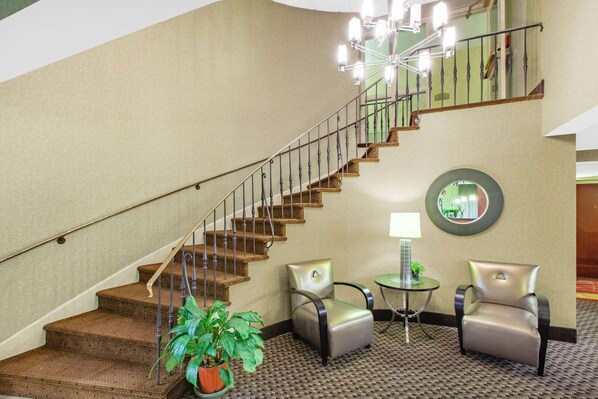 A staircase with a handrail, a potted plant, two armchairs, a small table with a lamp, and a mirror on the wall. - Baymont by Wyndham Harrisburg (Harrisburg)