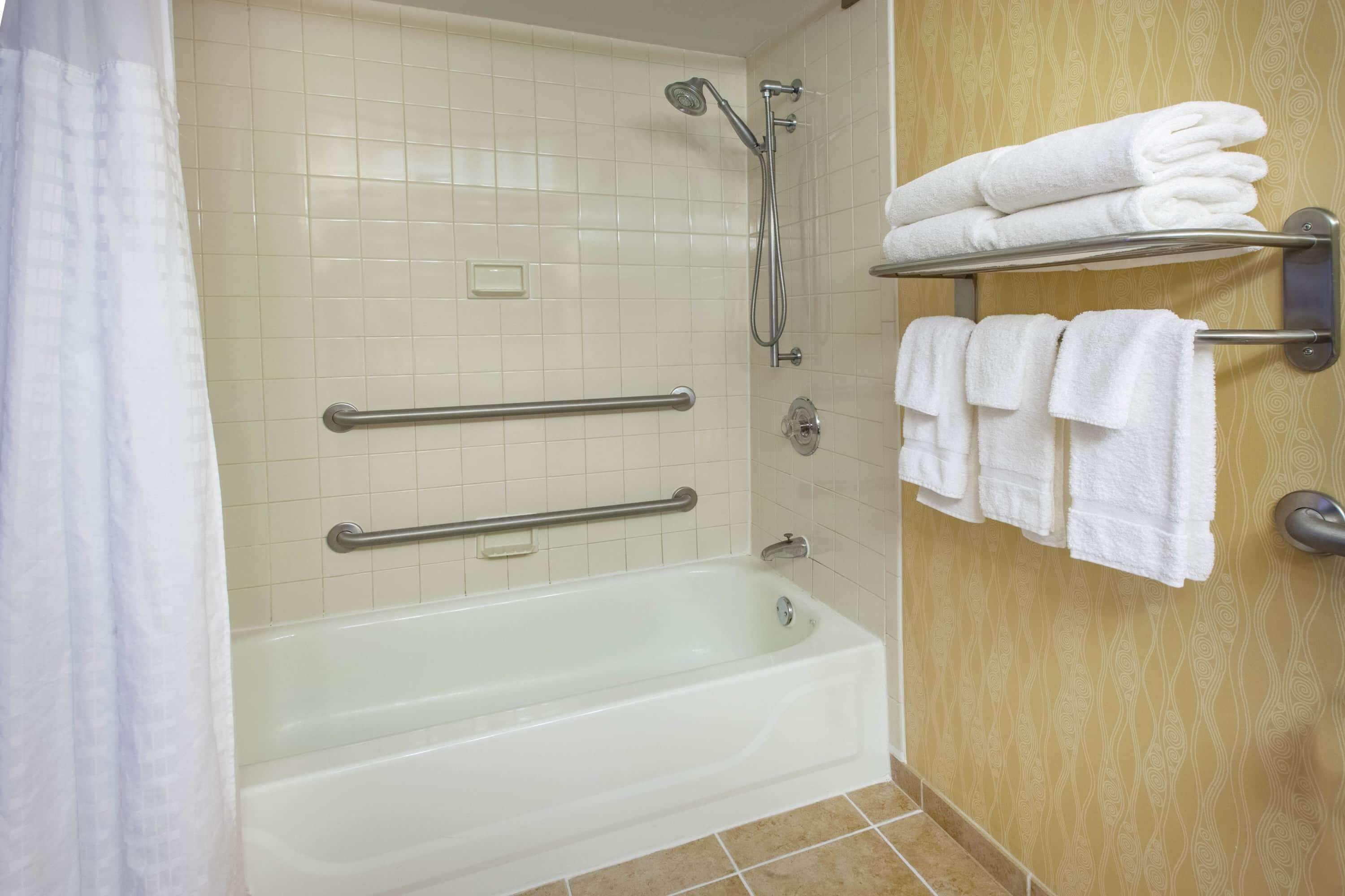 A bathroom with a bathtub, grab bars, a towel rack, and a showerhead.