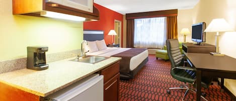 A hotel room with a bed, a desk, a chair, a television, a microwave, and a coffee maker.