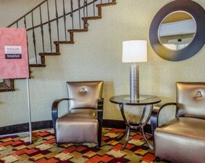 Hotellihuone, jossa on portaikko, kaksi nahkaista nojatuolia, pieni pyöreä pöytä lampun kanssa ja peili seinällä.