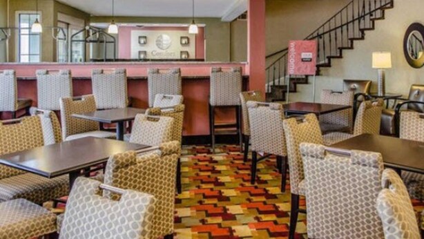 Un hall de hotel con mostrador de recepción, sillas y mesas con diseños, una escalera y una alfombra estampada.