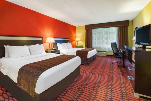 A hotel room with two beds, a desk, a television, and a window with curtains. - Baymont by Wyndham Harrisburg (Harrisburg)