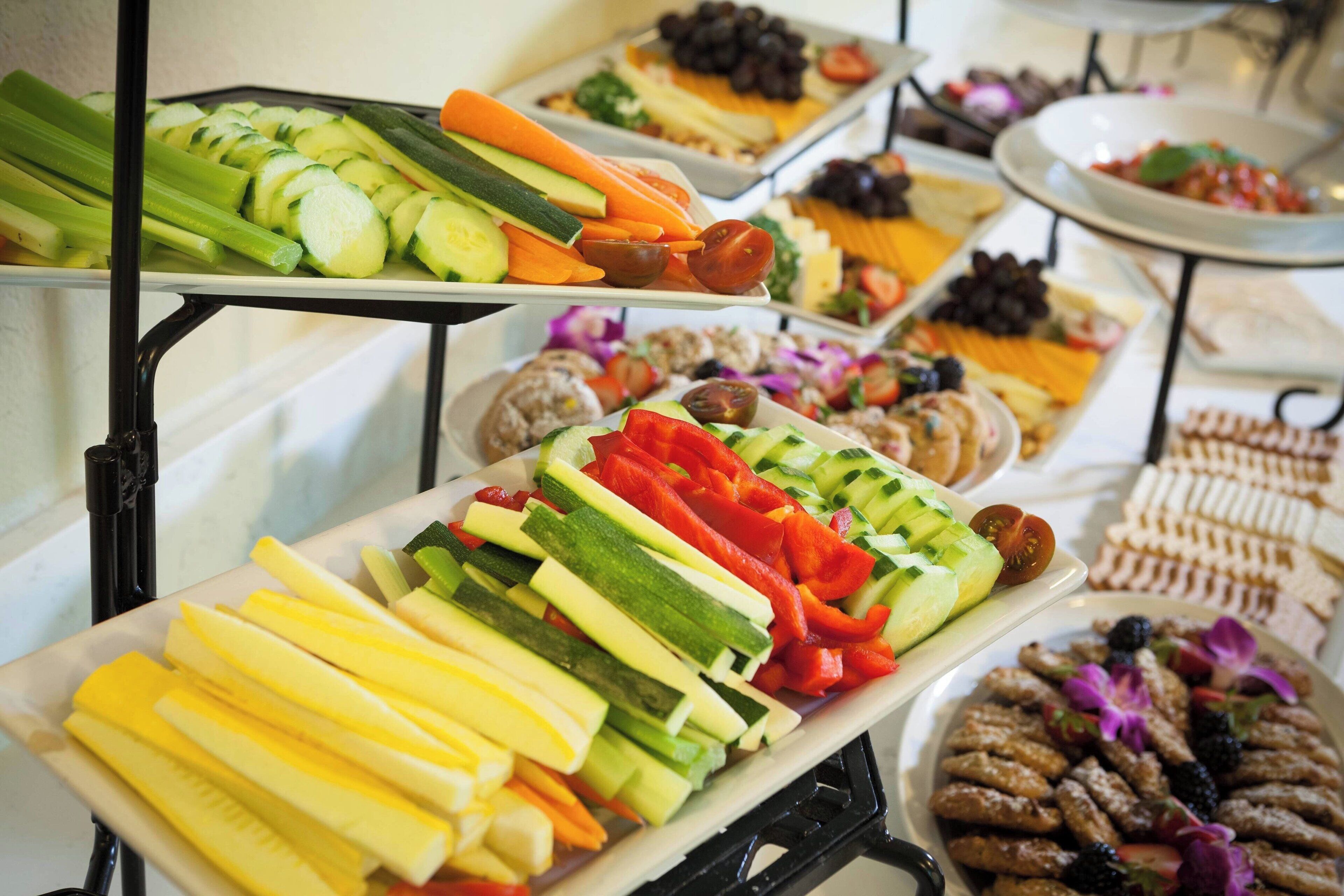 Buffet com diversos alimentos, incluindo legumes fatiados, carnes e queijos.