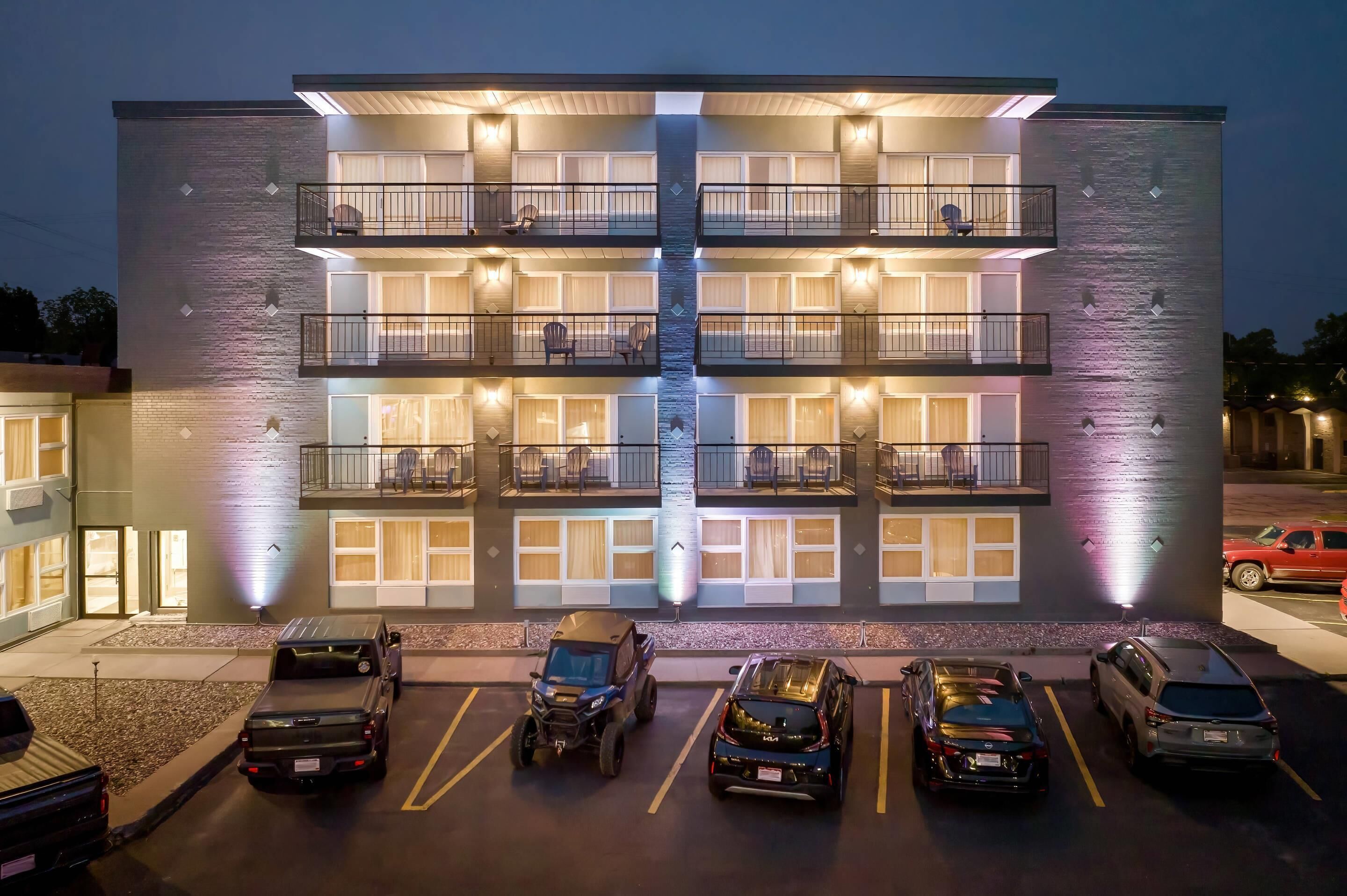 Un hotel de varios pisos con balcones, una fuente central y un estacionamiento con varios vehículos.