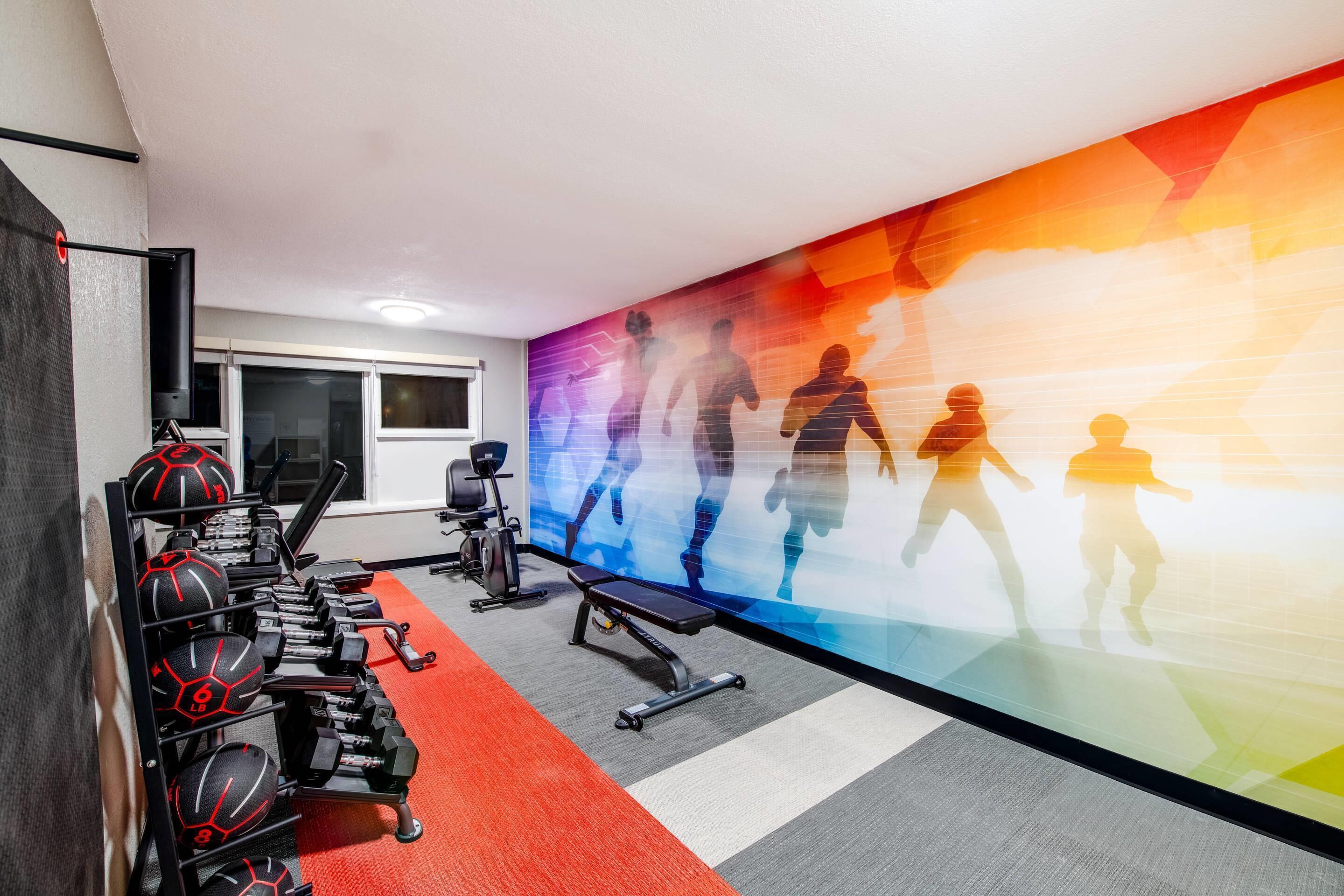 A gym with exercise equipment, a wall with silhouettes of people exercising, and a window.