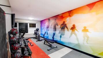 Un gimnasio con equipo de ejercicio, una pared con siluetas de personas haciendo ejercicio, y una ventana.