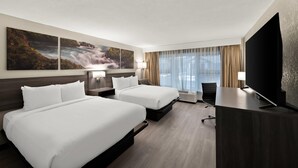 Une chambre d’hôtel avec deux lits, un bureau, une télévision et de grandes fenêtres équipées de rideaux.