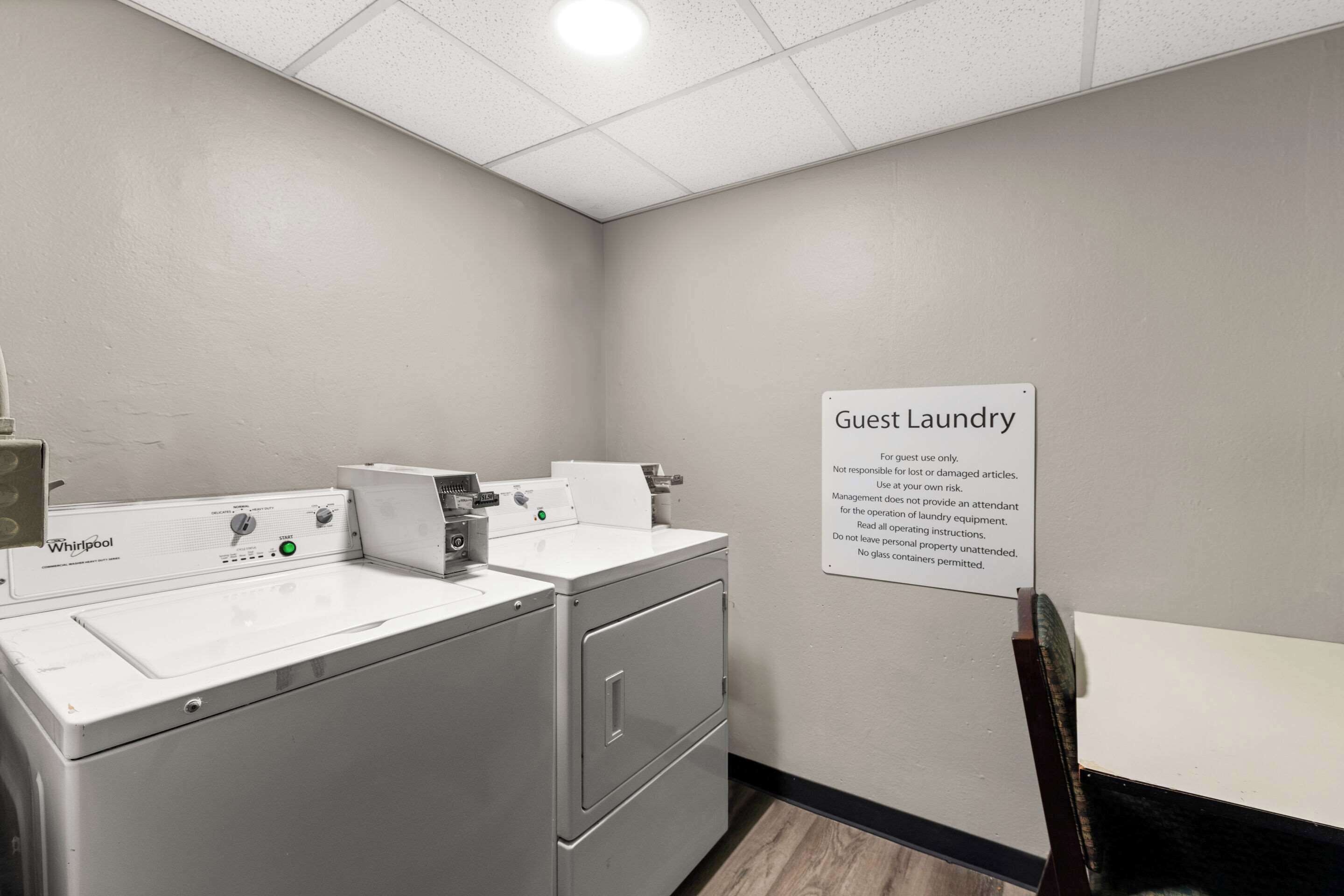 A guest laundry area with Whirlpool washers and dryers, a sign with usage instructions, and a small table.