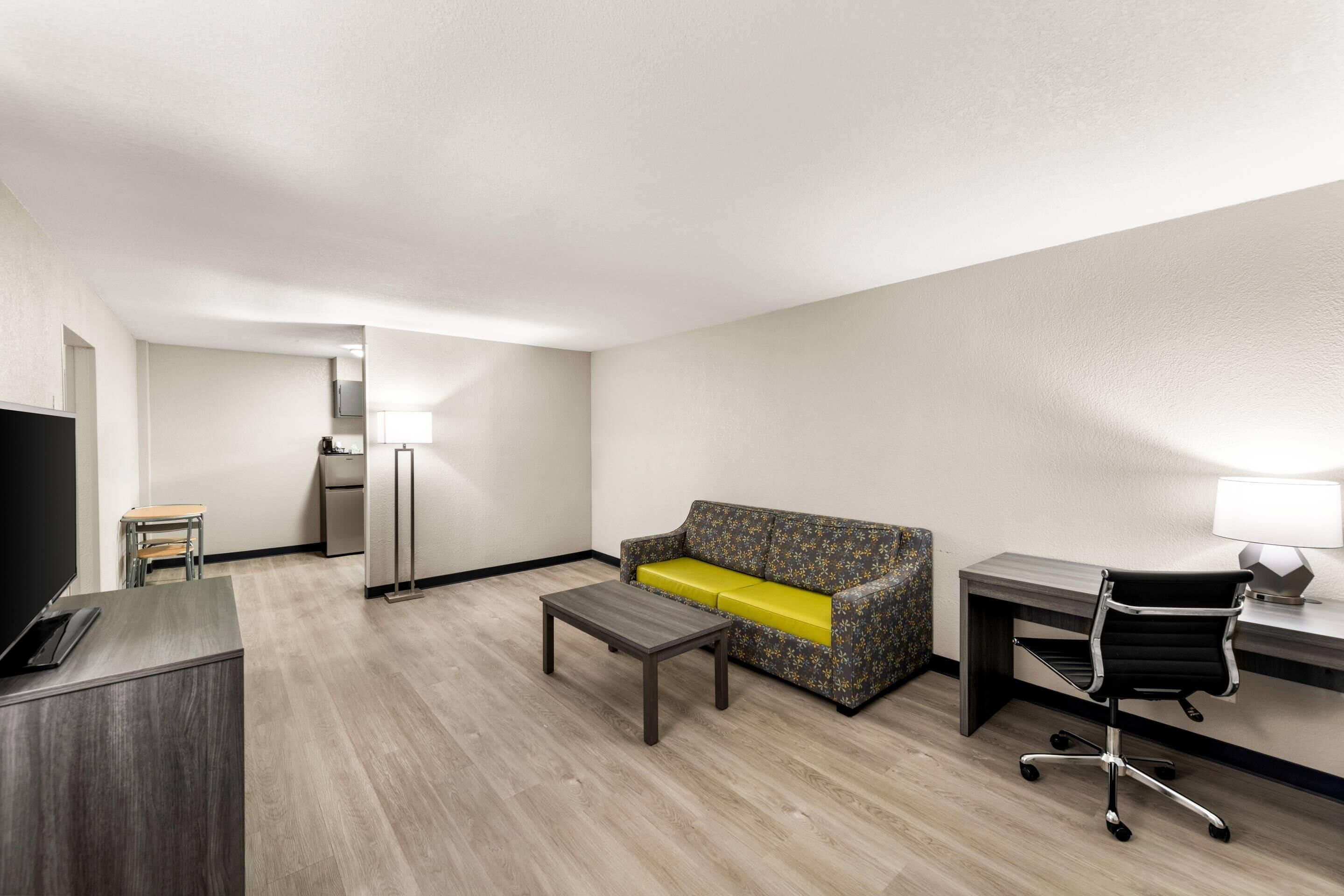 A hotel room with a sofa, a desk, a chair, a TV, and a lamp.