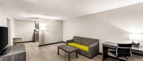 A hotel room with a sofa, a desk, a chair, a TV, and a lamp.