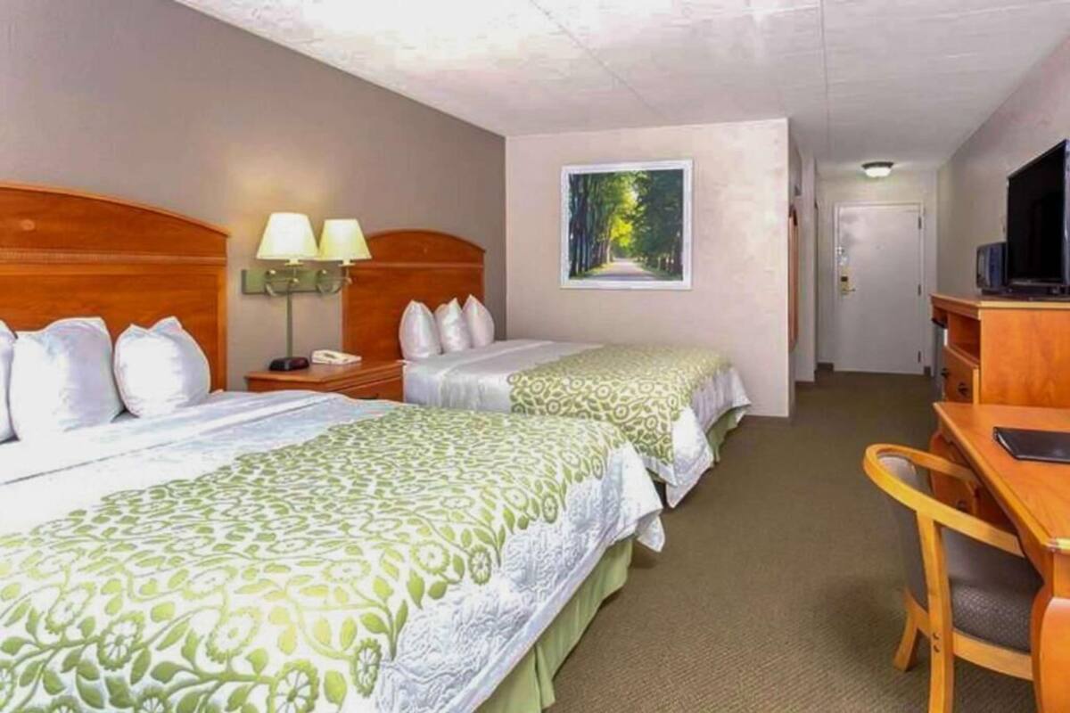 A hotel room with two beds, a desk, a chair, a television, and a painting on the wall.