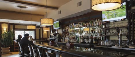 A bar area with a long counter, multiple hanging lamps, and a television screen displaying a landscape.