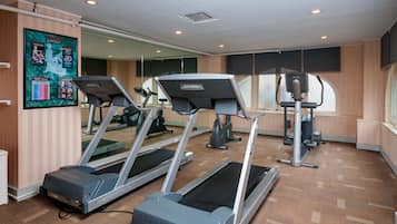 Un gimnasio con cintas de correr, un espejo grande y un cartel que muestra rutinas de ejercicio.