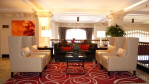 A hotel lobby with a red patterned carpet, two white armchairs, a sofa with red cushions, a coffee table, and a large painting on the wall. - The Pickwick Hotel (San Francisco)