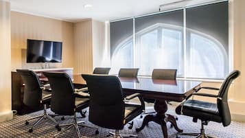 A conference room with a large table, six chairs, a flat-screen TV, and a large window with a view of the city.