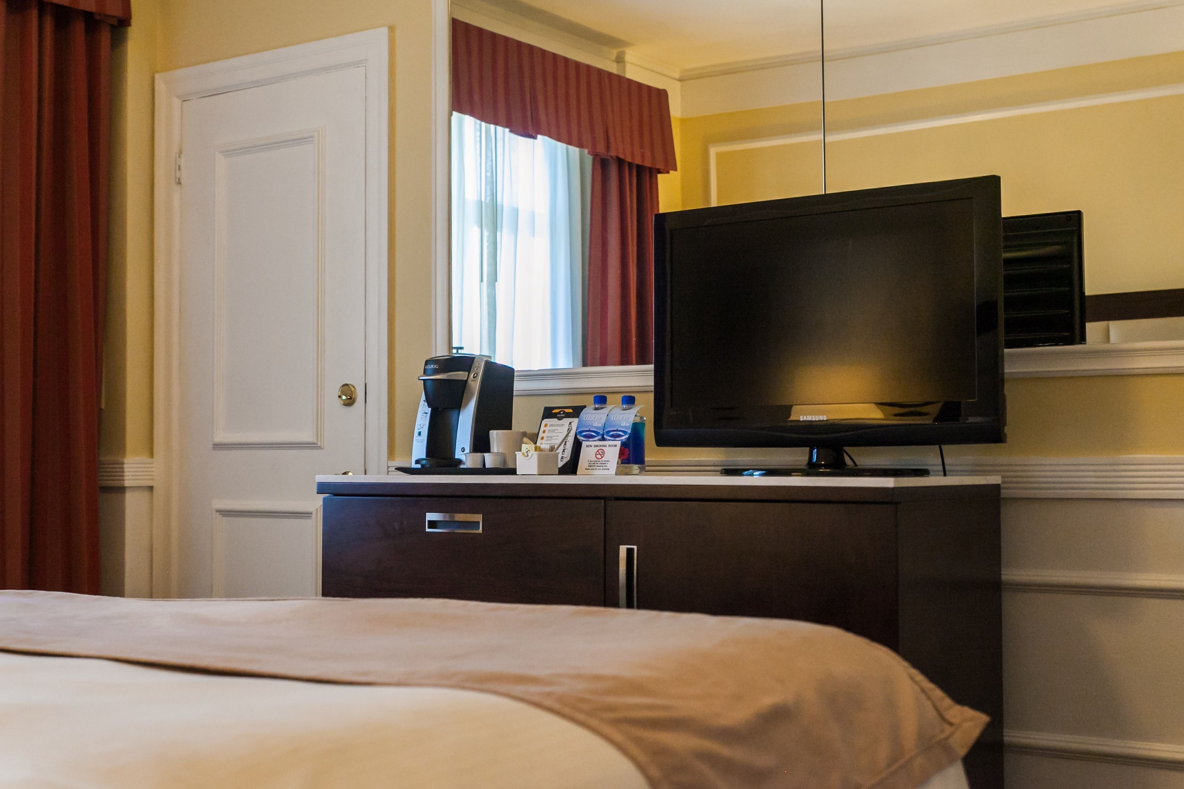 A hotel room with a bed, a television on a stand, a coffee maker, and a minibar.
