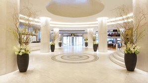 Un amplio hall con piso de diseño circular, columnas imponentes y plantas en macetas.