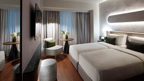 Una habitación de hotel moderna con una cama grande, un área de descanso con una mesa redonda y un espejo que refleja la habitación.