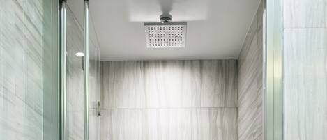 Une douche moderne dotée d’une porte en verre, d’un pommeau de douche à main, d’un robinet mural et d’un distributeur de savon.