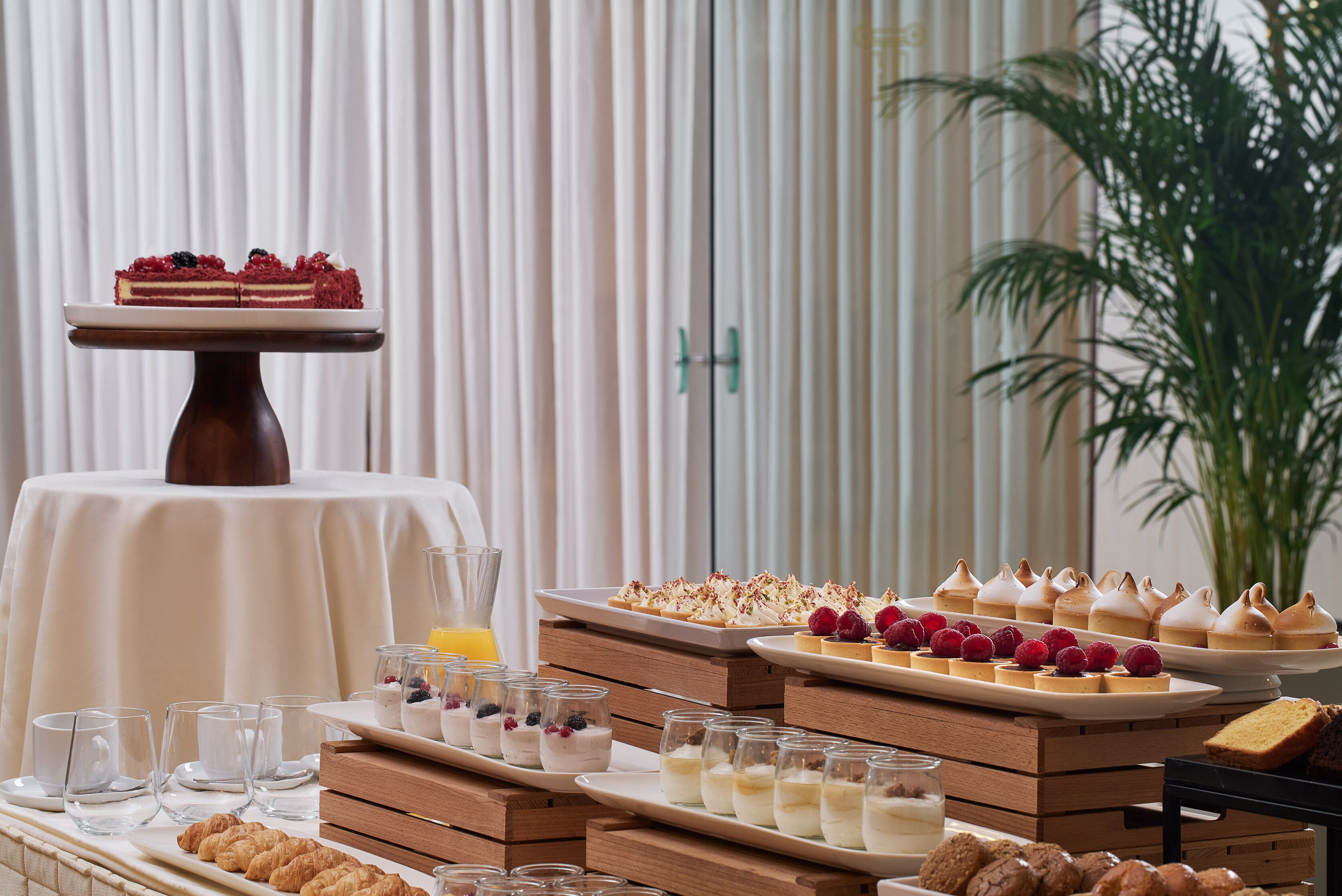Una mesa de buffet con diversos postres y pasteles, incluyendo un pastel con frutos rojos, dispuesta sobre pedestales y platos de madera.