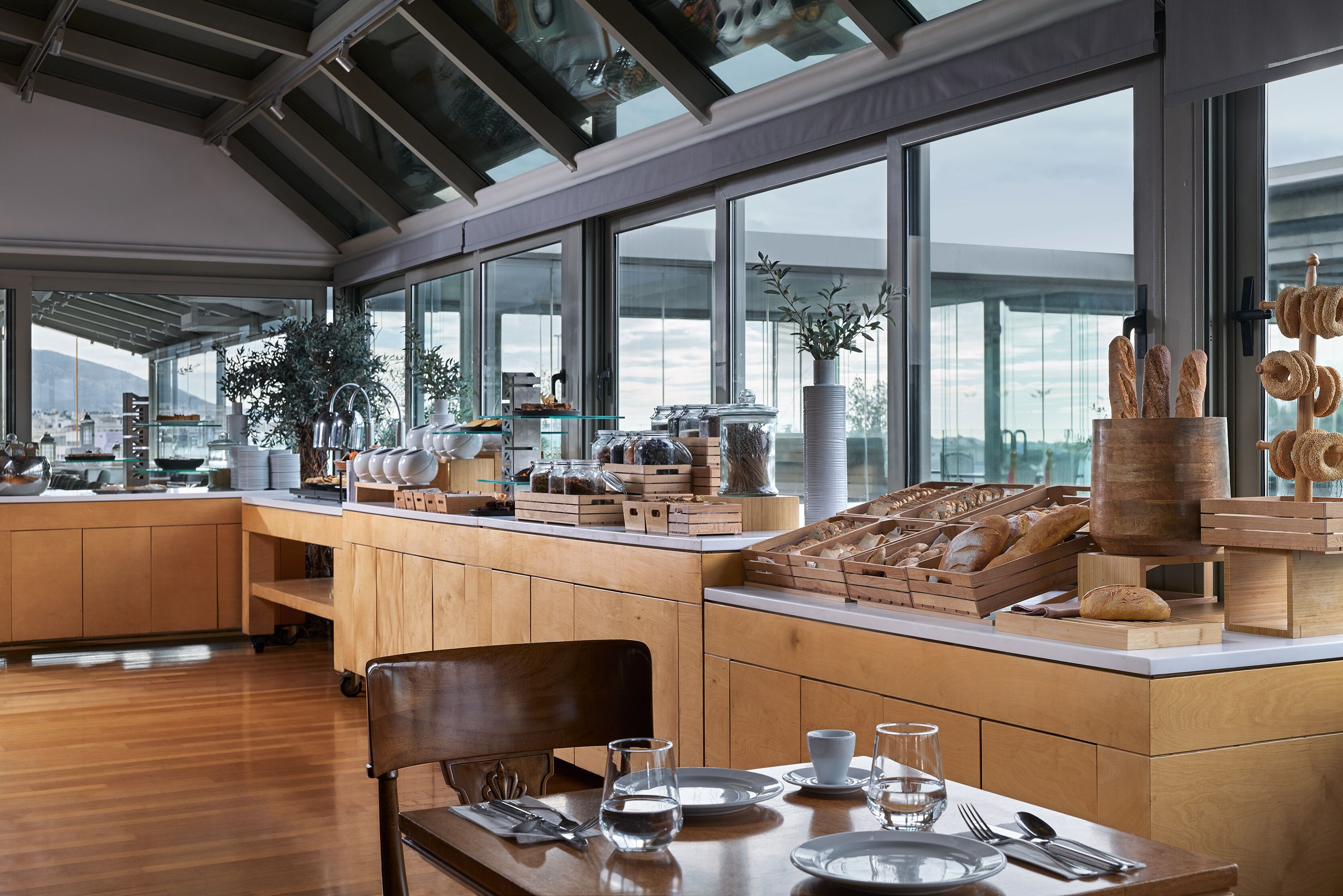 A modern kitchen with wooden cabinets, a dining area with a table set for two, and a large window with a view of the city.